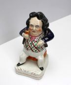 A Staffordshire figure of a seated portly figure with his hand in his waistcoat pocket, on a