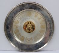 A silver Arms dish, of circular form, the central gilt roundel moulded with the Queen on the throne,
