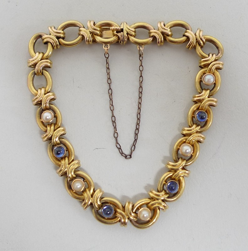 A 14ct gold fancy link bracelet set to nine links with cabochon sapphires and seed pearls on a
