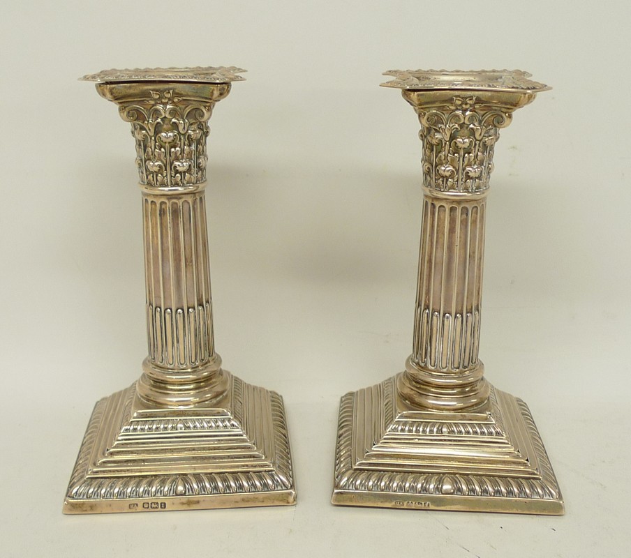 A pair of silver loaded candlesticks of Corinthian column form, raised on square stepped and