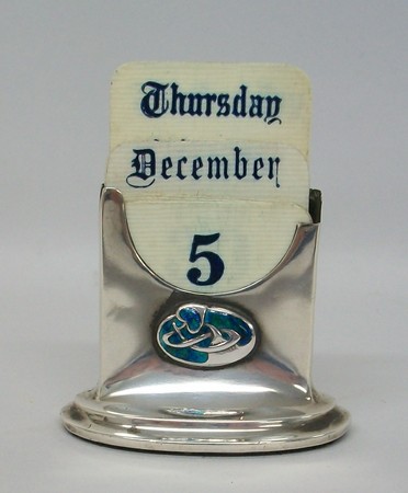 A Denkin & Francis silver desk calendar, containing ivorene cards, set with an enamel Celtic knot,