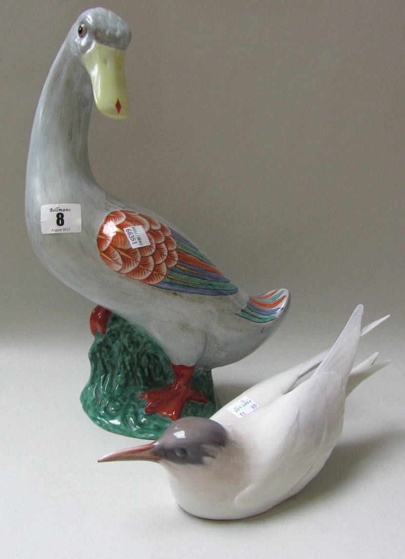 A porcelain figure of a duck, with grey plumage and coloured wings, standing on a naturalistic green