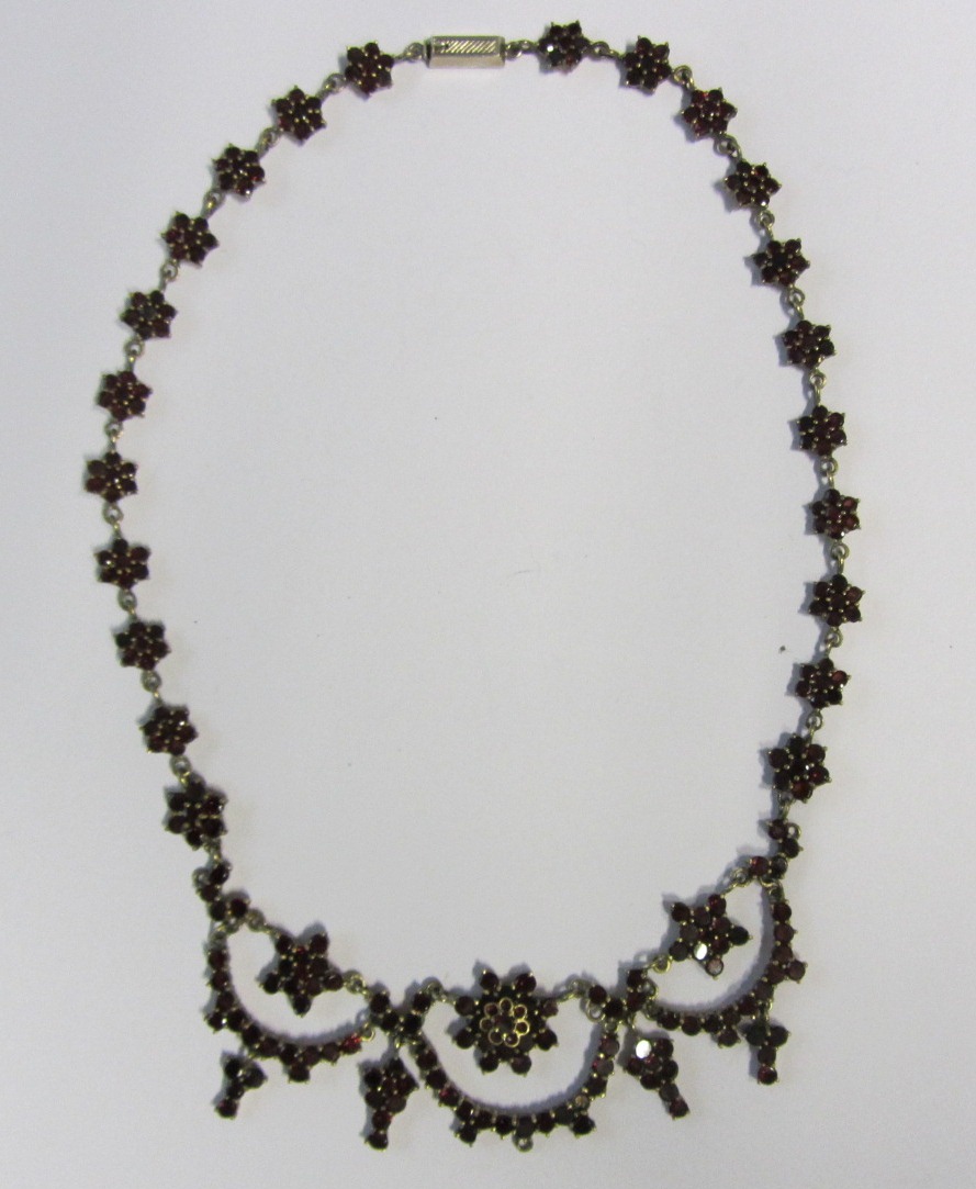 A garnet set necklace, designed as a row of graduated flowerhead shaped clusters and with drops to