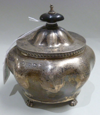 A silver tea caddy, of compressed oval form, with an ebonised finial to the hinged lid, raised on