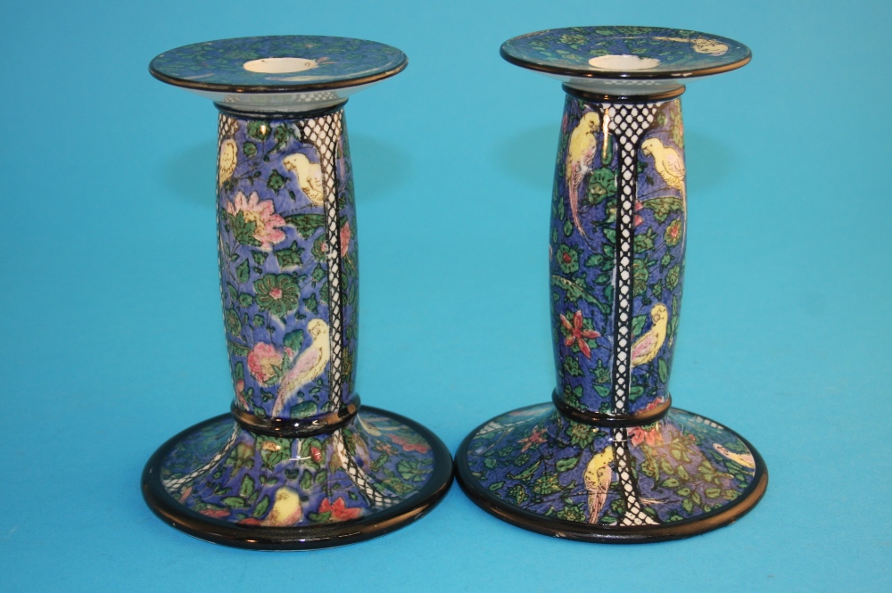 A pair of Royal Doulton candlesticks on a blue ground decorated with parakeets, printed mark,