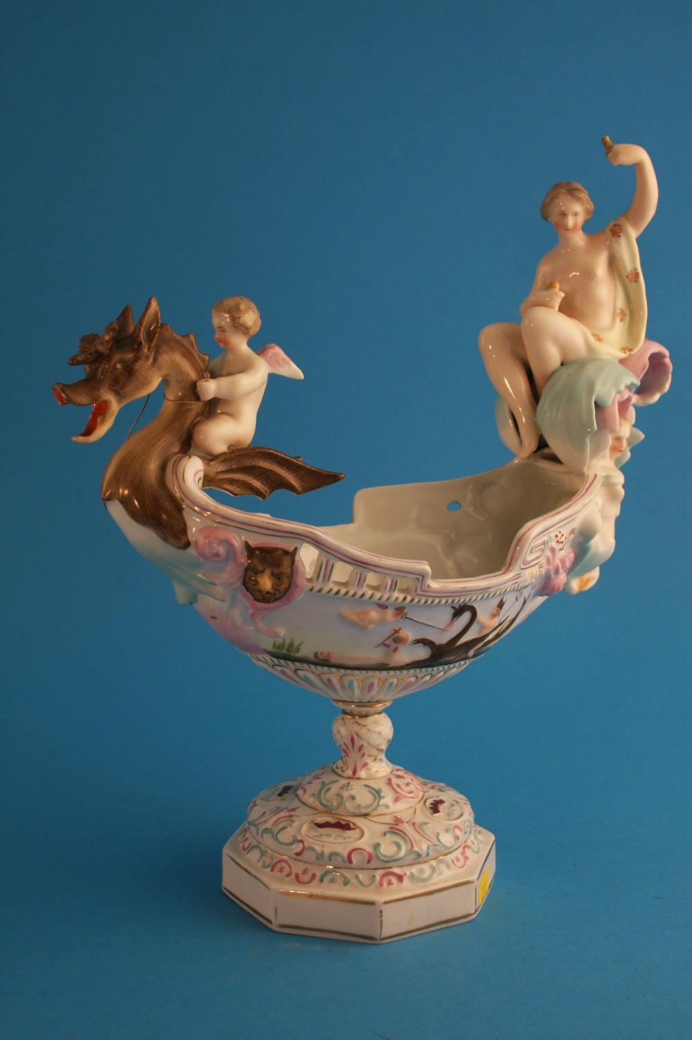 A Continental porcelain centrepiece in the form of a boat shaped dish surmounted with semi-naked
