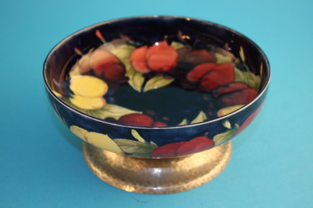 A shallow Moorcroft circular bowl decorated with pomegranates on a dark blue ground supported on a