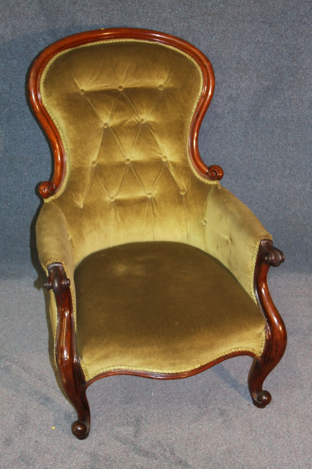 A Victorian mahogany button back chair with swept scrolling arms, supported on cabriole legs.