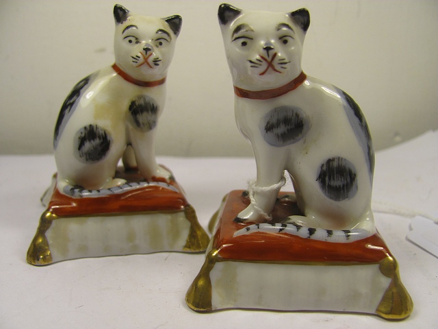 A pair of early 20th century porcelain gold anchor mark cats sitting on red cushions, 3" high.