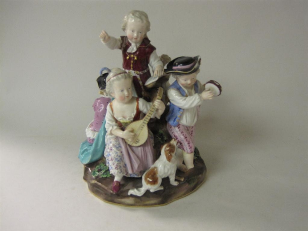 A Meissen figure of children musicians seated on rustic tree trunk, one with dog at foot, firing and