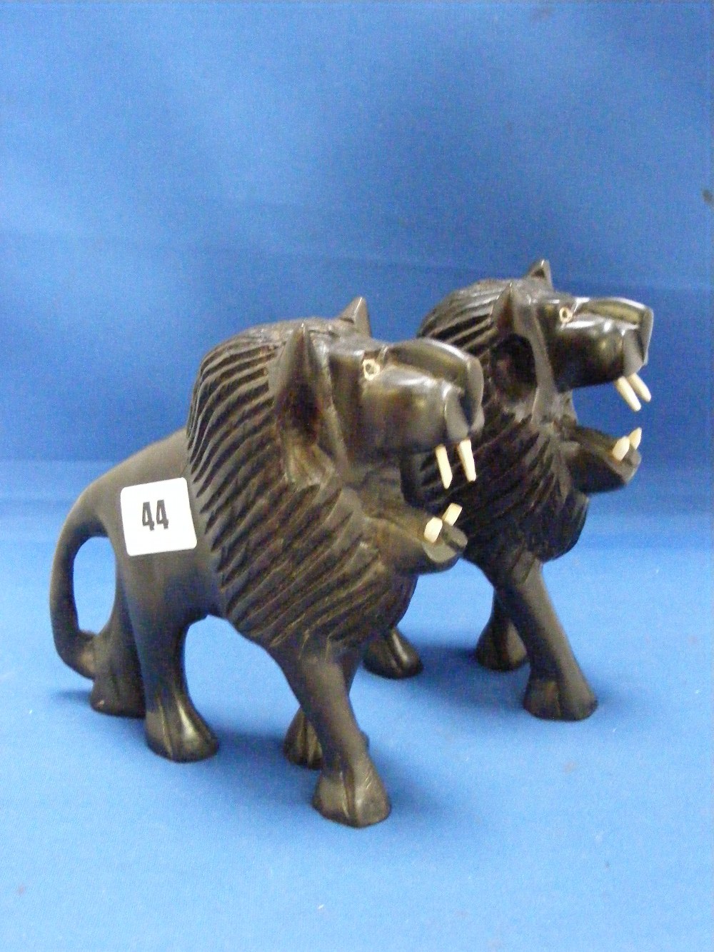 A pair of ebony carved figures of lions with ivory teeth and eyes.