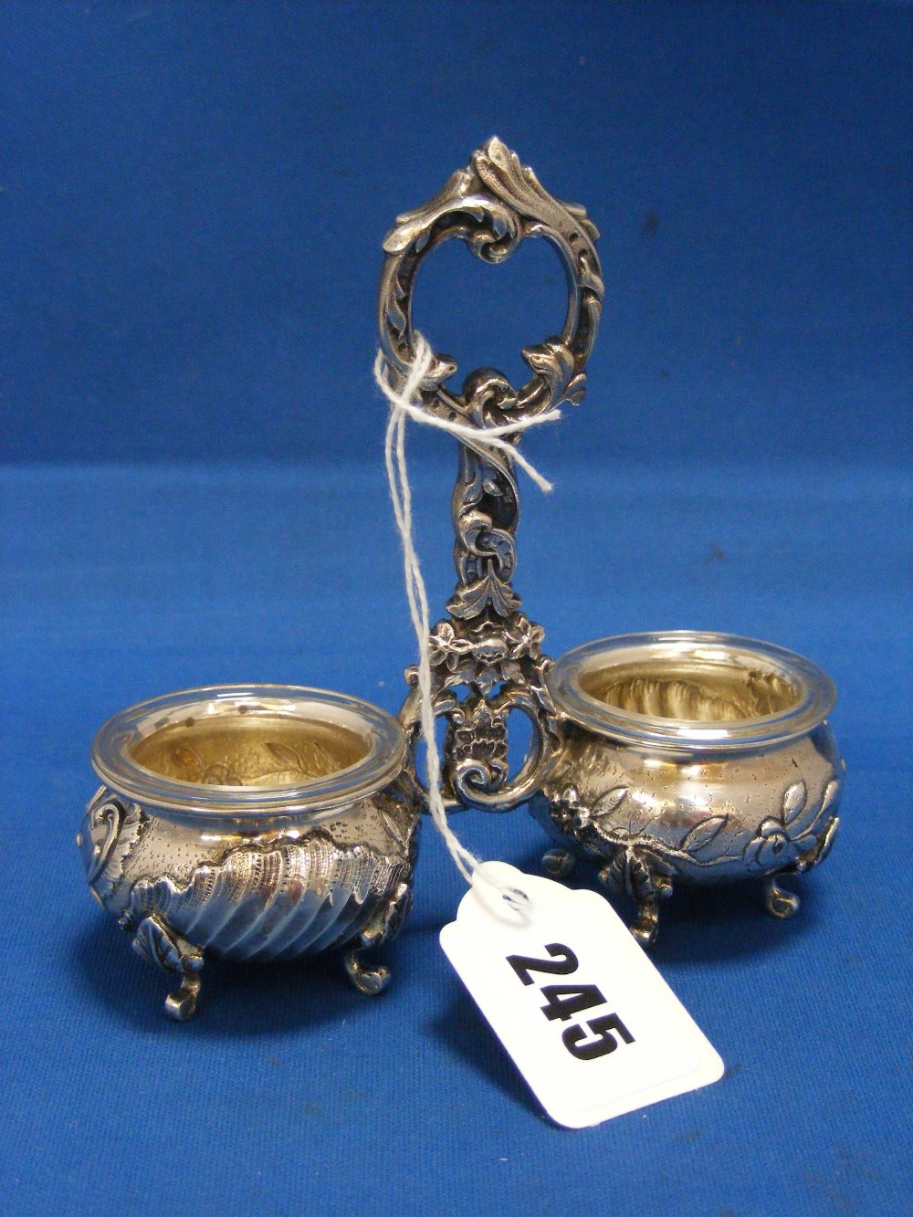 A fine quality French silver twin salt holder, the supporting handle of ornate form and the salts