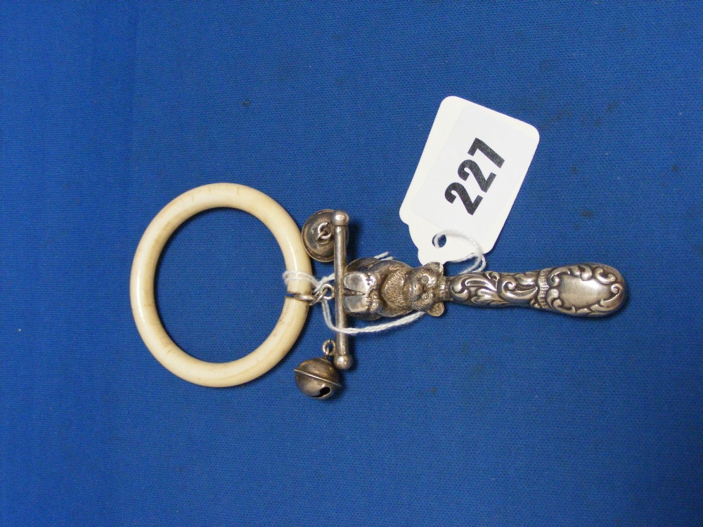 An Edwardian English silver baby's rattle with a decorative handle surmounted with a seated teddy
