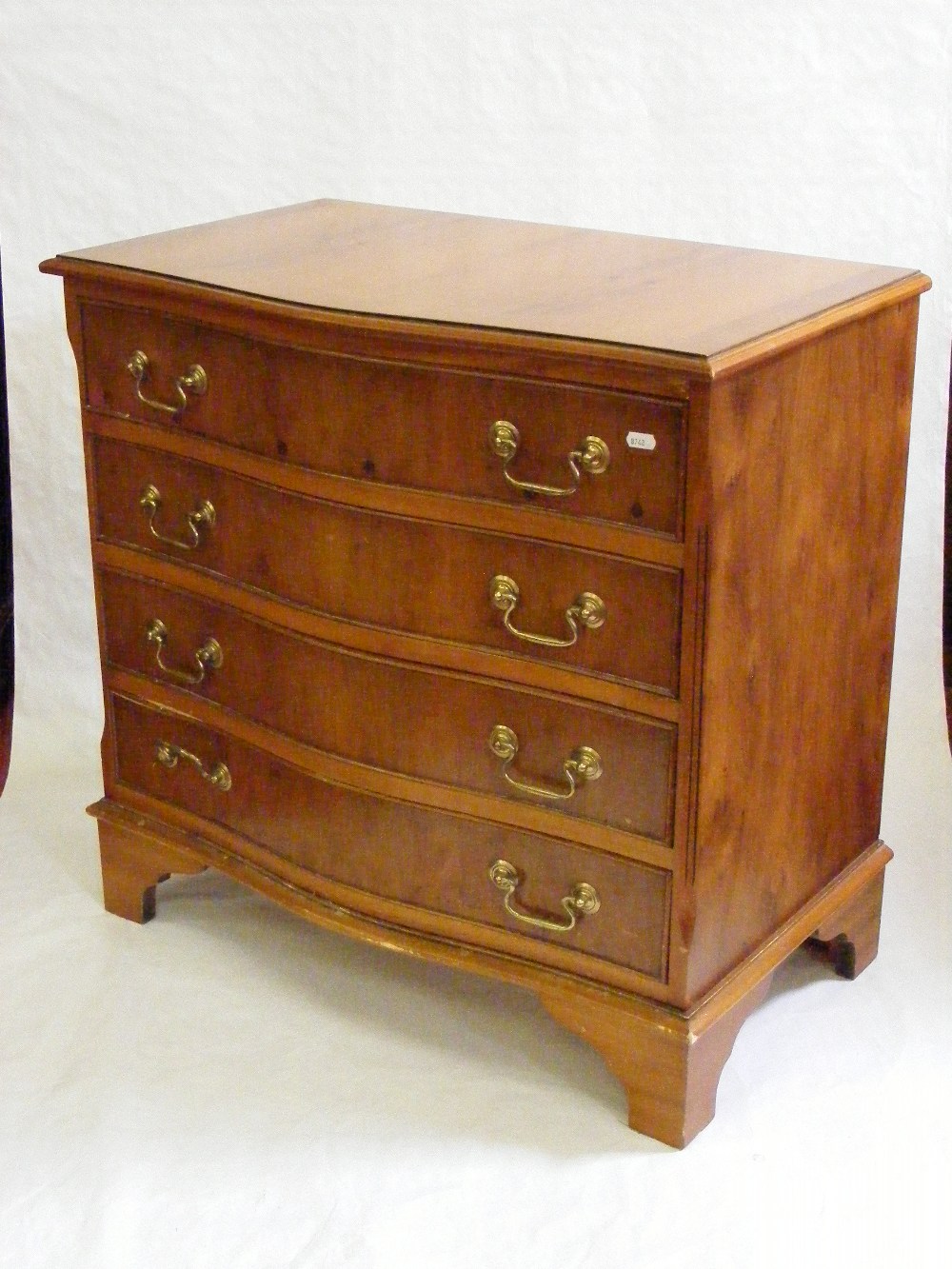A yew wood reproduction bow fronted chest of four shaped drawers on bracket supports.