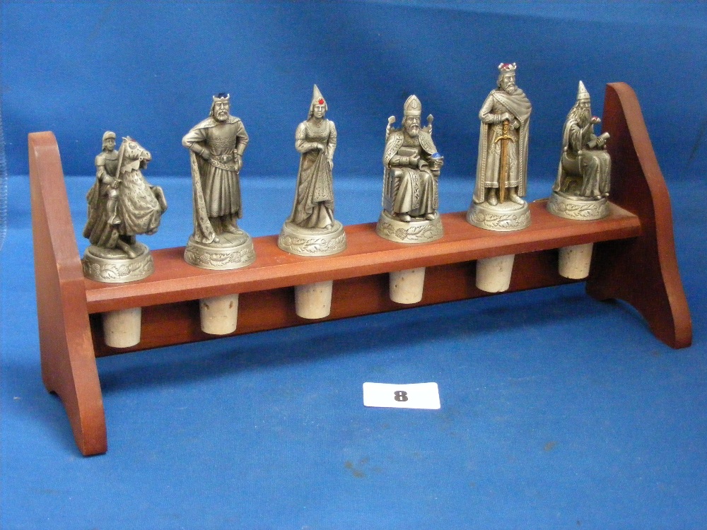 A wooden rack display of six pewter bottle stoppers, each one depicting Arthurian characters.