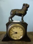 A pewter clock with a figure of a dog mounted to the top