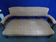 An Edwardian salon sofa being covered in a brown fabric, the arms and back rail being on decorated