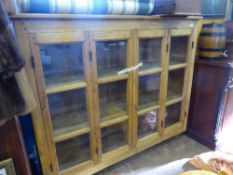 A French pine glass fronted credenza having two folding hinged doors enclosing three shelves on