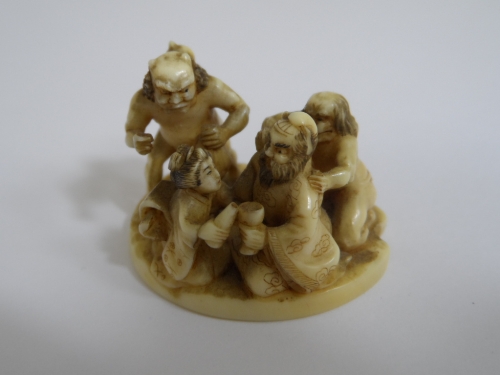 Japanese ivory Netsuke in the form of a couple seated with malevolent characters on either side, two