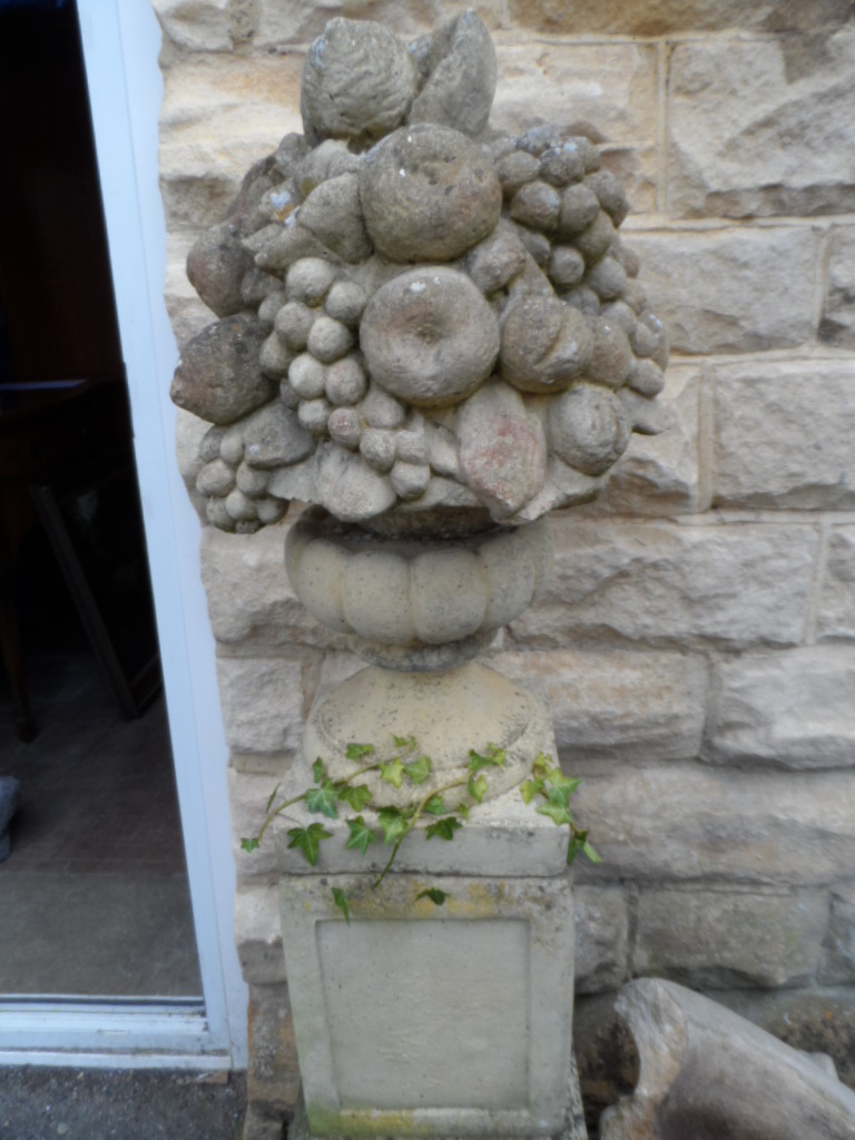 A Stone Garden Ornament being decorated with fruit on a plinth.