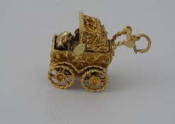 A 9 ct Gold Charm. The charm being in the form of an ornate pram with folding hood, revolving wheels