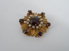 Garnet and Pearl Brooch, The 9 ct yellow gold brooch set as a flower having central garnet