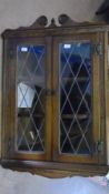 AN OLD CHARM OAK WALL HANGING CABINET HAVING LEADED LIGHT GLAZING WITH CARVED AND SHAPED