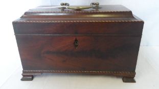 A MAHOGANY INLAID GEORGIAN STYLE TEA CADDY WITH RIBBON INLAID TOP AND FACE ON BRACKET FEET