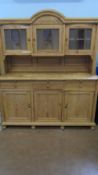 A LARGE ANTIQUE PINE DRESSER, THE TOP HAVING THREE GLAZED DOORS, THE TWO SIDE DOORS BEING BOW