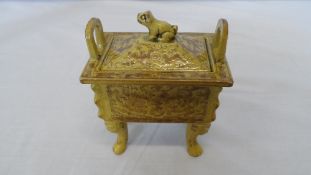 A CERAMIC MUSTARD YELLOW LIDDED SENSER, DEPICTING A MALEVOLENT CHARACTER ON FOUR SIDES FLANKED BY