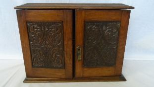 AN OAK CARVED SMOKING CHEST WITH TWO CARVED PANELS TO THE FRONT DOORS - THE INTERIOR HAVING TWO