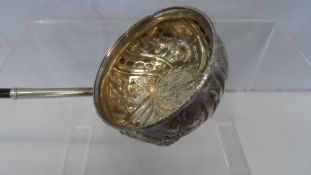 AN ANTIQUE SILVER BRANDY LADLE WITH TURNED EBONY HANDLE, THE LADLE BEING EMBOSSED WITH FLOWERS