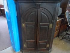 AN ANTIQUE OAK CORNER CABINET, HAVING TWO ARCHED PANELLED DOORS ON BRACKET FEET WITH REEDED