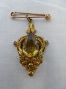 A YELLOW STONE PENDANT SET IN A FANCY FILIGREE SETTING ON A 9 CT GOLD PIN.