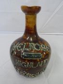 A DOULTON LAMBETH WARE BROWN MOTTLED GLAZED POTTERY SPIRIT BOTTLE HAVING MELROSE HIGHLAND WHISKY