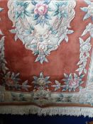 A WASHED CHINESE WOOL CARPET - RUST COLOURED WITH FLORAL BORDER AND A SIMILAR DIAMOND PATTERN TO