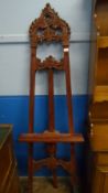 A VICTORIAN MAHOGANY ARTIST`S FOLDING EASEL HAVING ORNATELY CARVED DECORATION TO THE TOP AND BOTTOM,
