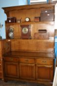 AN OAK EFFECT STAG DRESSER WITH TWO PLATE RACKS WITH DRAWERS AND CUPBOARDS UNDER ON BRACKET FEET,