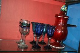 A RUBY GLASS LIDDED VASE WITH MURANO STYLE FLOWERS TO TOP TOGETHER WITH FOUR BLUE GLASS WINE GOBLETS