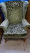 A PARKER KNOLL WING BACK ARMCHAIR HAVING CABRIOLE FEET TO THE FRONT AND BEING UPHOLSTERED IN A GREEN