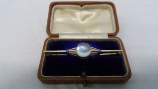 A LADY`S YELLOW GOLD ENAMEL AND MOONSTONE BAR BROOCH, THE BROOCH SET WITH A CABOCHON MOONSTONE