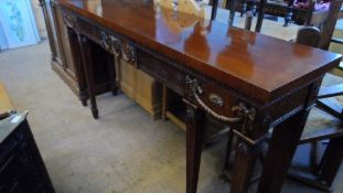 A REGENCY STYLE MAHOGANY SIDEBOARD ON REEDED LEGS, THE SIDEBOARD HAVING AN ADAMS STYLE FRONT