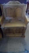 A SMALL PINE SETTLE HAVING A HINGED SEAT WITH PANELLED FRONT AND CARVING TO FRONT SUPPORTS,