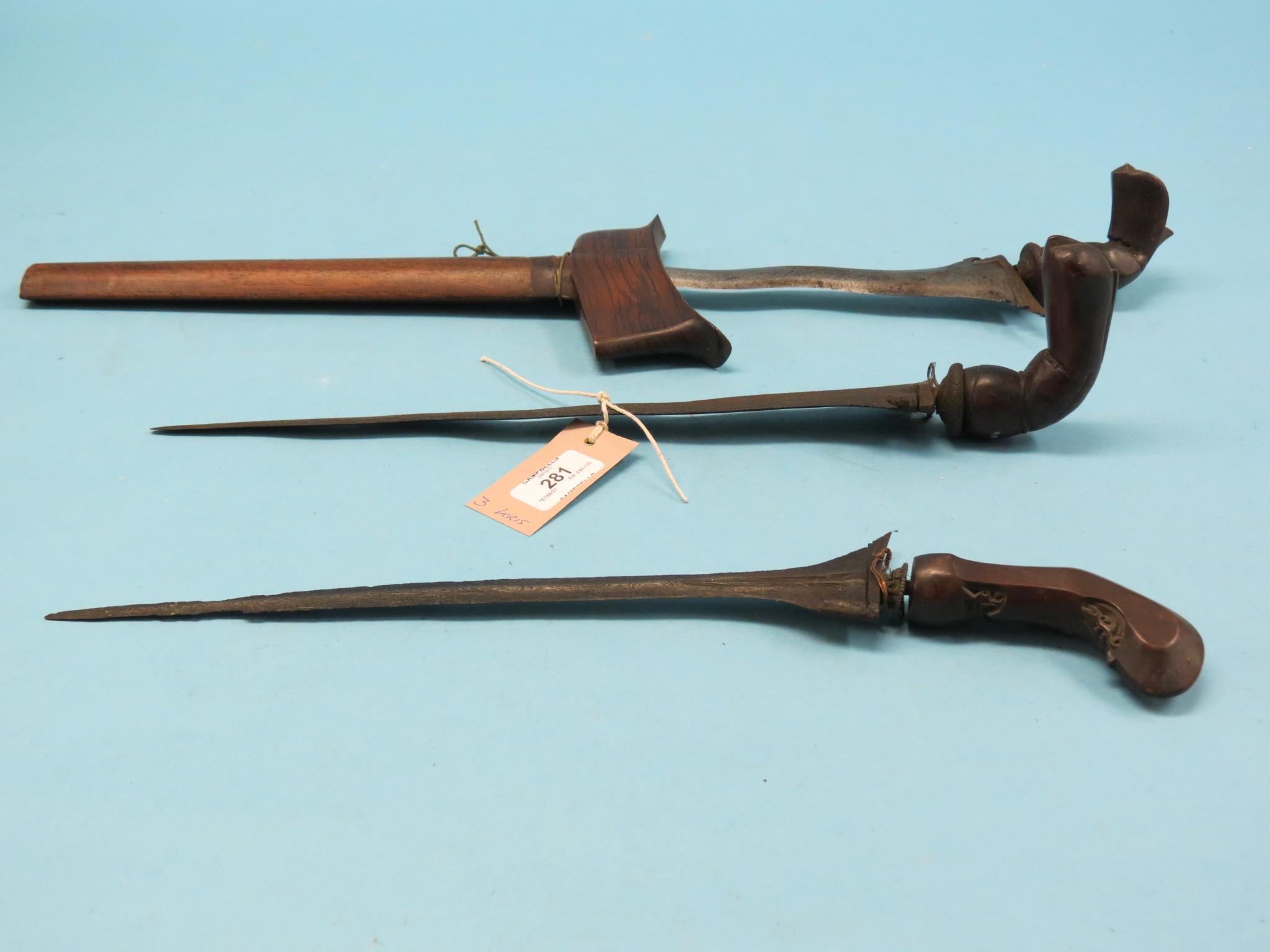 Three kris, each with curved, double-edged blade and carved wood handle, one within sheath