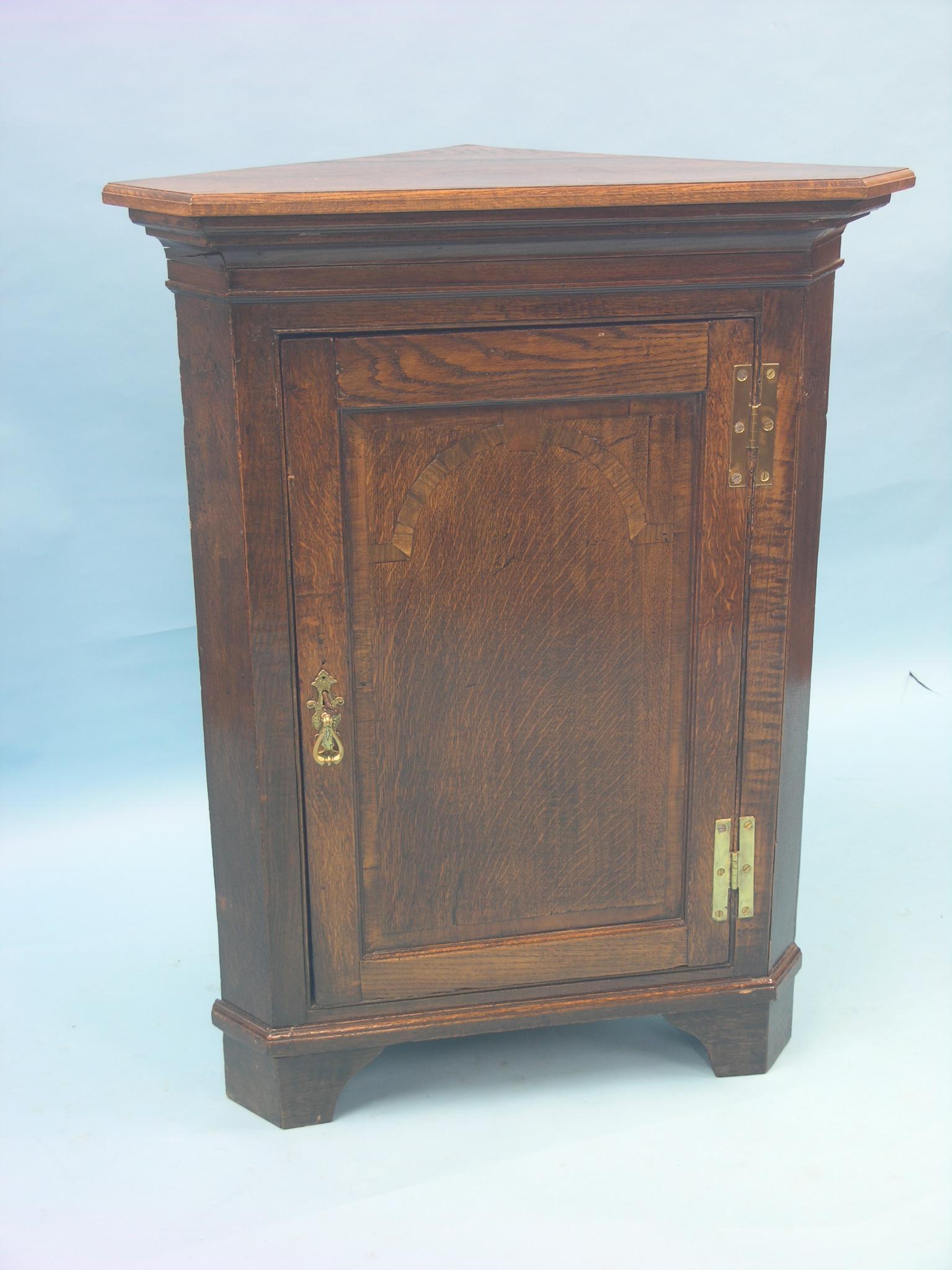 A late Georgian oak corner cupboard, floor-standing, enclosed by single panelled door with walnut