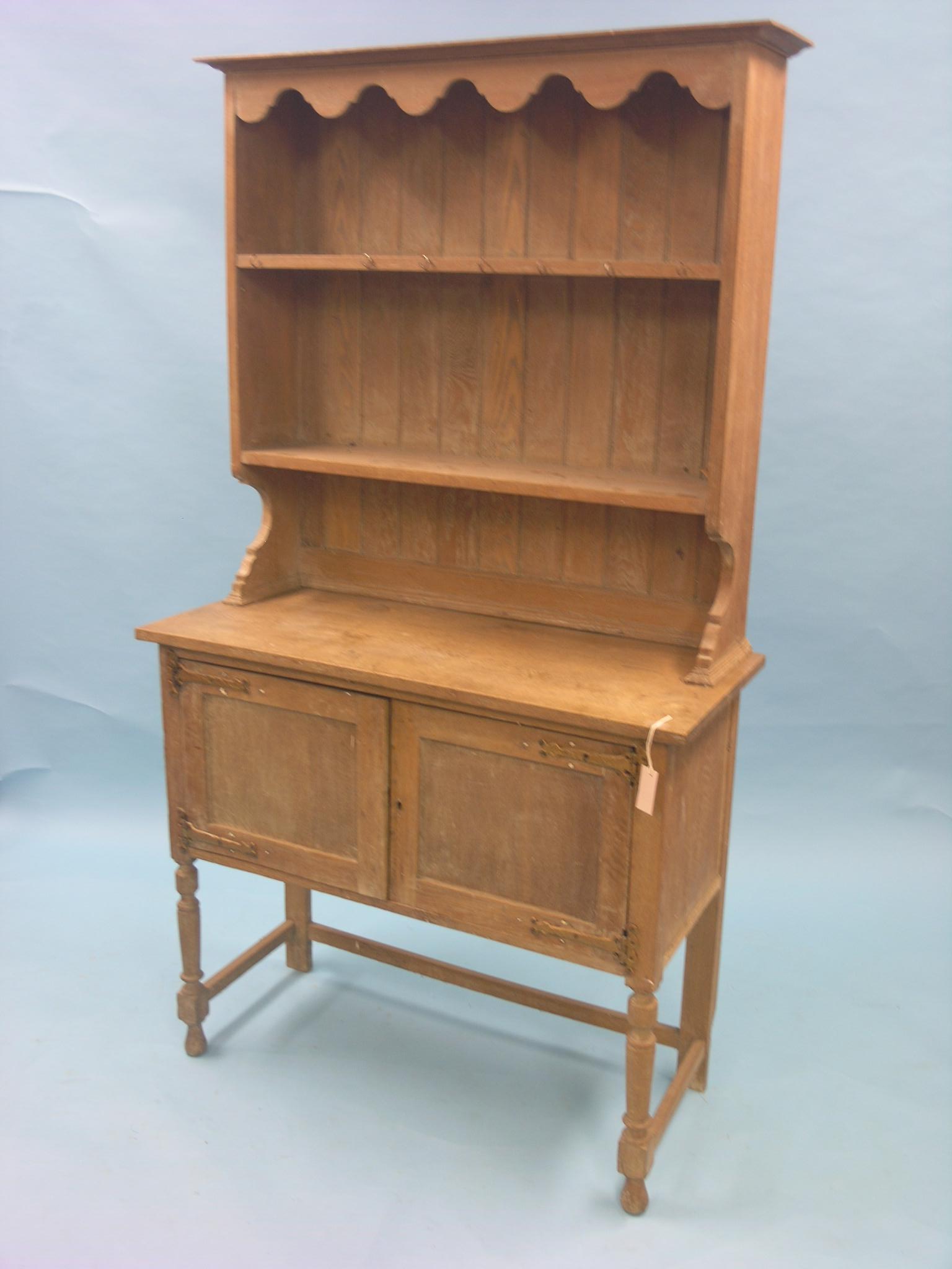 A solid, limed oak dresser, twin-shelf plate rack above panelled cupboard base, front turned legs,