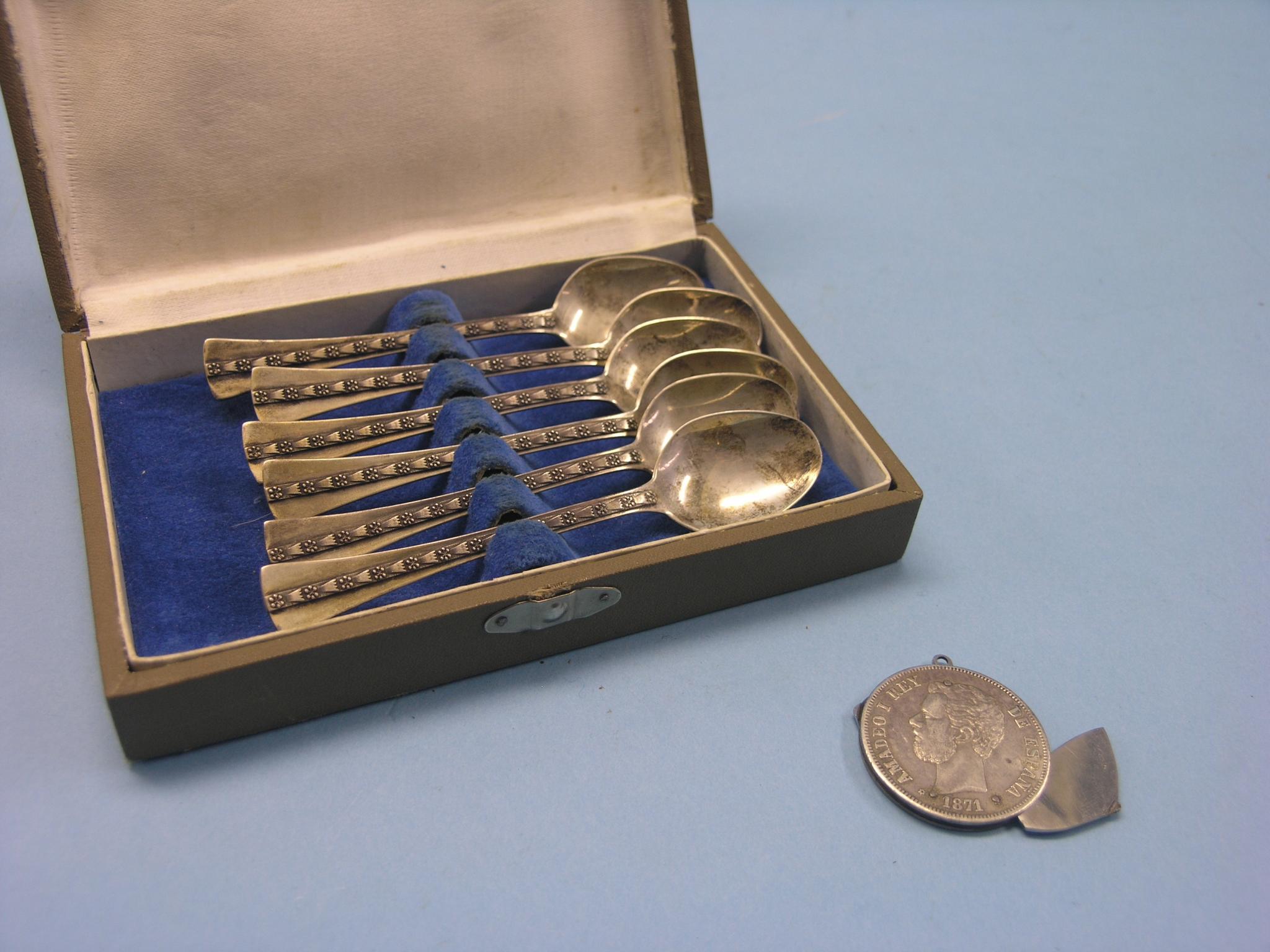 A cased set of six white metal teaspoons and a Spanish five Pesetas silver coin, 1871, modified to