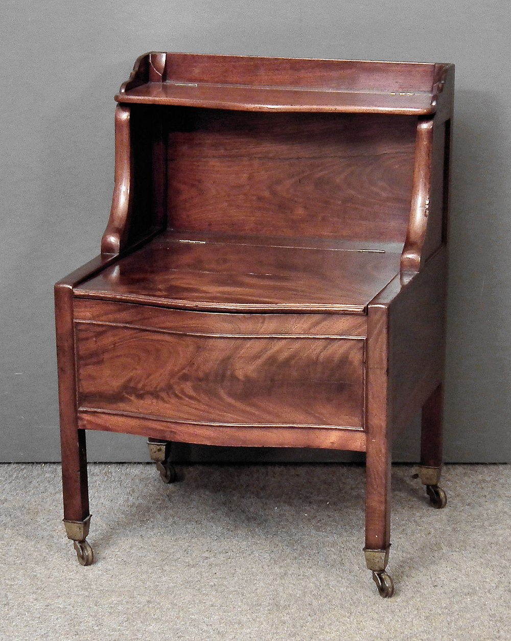 A George III mahogany serpentine fronted tray top bedside commode, with lifting seat, on square legs