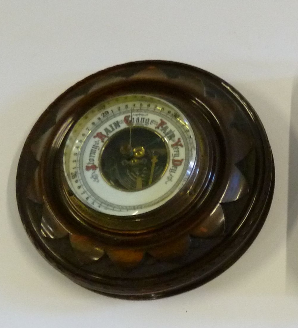 EDWARDIAN CARVED WALNUT CIRCULAR ANEROID BAROMETER having white enamelled dial, the centre with