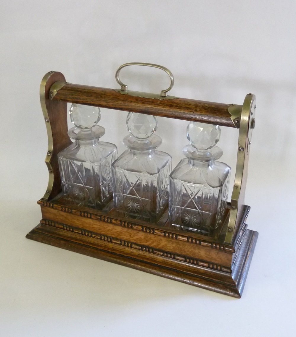 EARLY TWENTIETH CENTURY OAK FRAMED TANTALUS with E.P.N.S. mounts, having three square cut glass